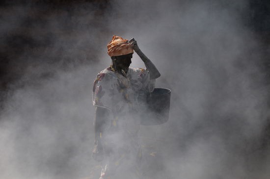 una donna va a raccogliere l'acqua attraversando i fumi emessi da una discarica - picking up water through garbage fired smog